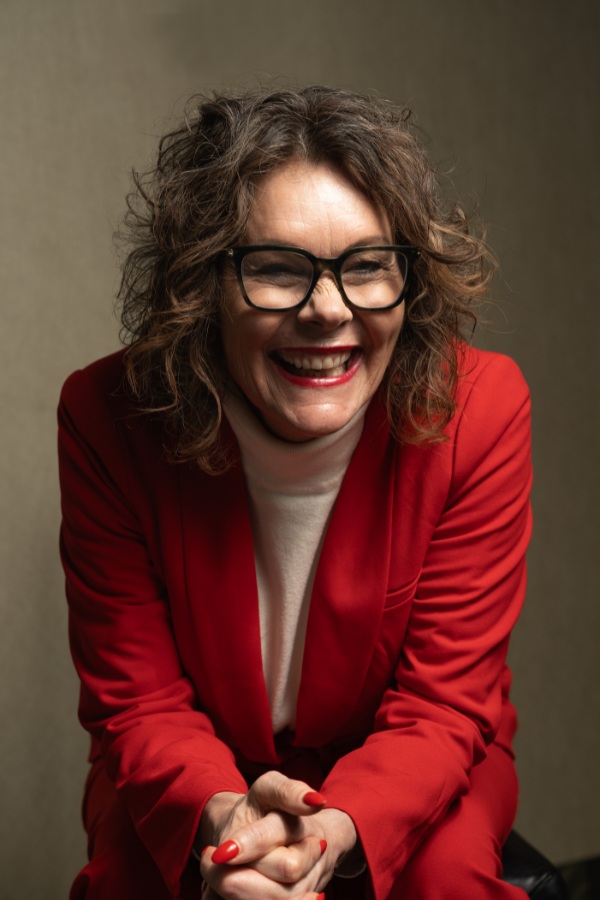 Tracy in a red outfit, sitting and laughing.